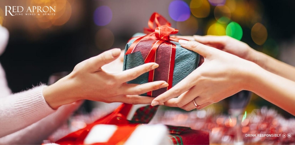 Hộp quà hình chữ nhật gói giấy xanh nhạt với nơ đỏ, cảnh trao tặng quà trong không gian ánh đèn ấm, gợi ý nâng cấp quà Tết trang trọng