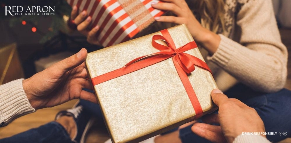 Hai người đang trao tặng hộp quà gói giấy vàng với nơ đỏ, gợi ý màu sắc phong thủy khi làm quà Tết handmade