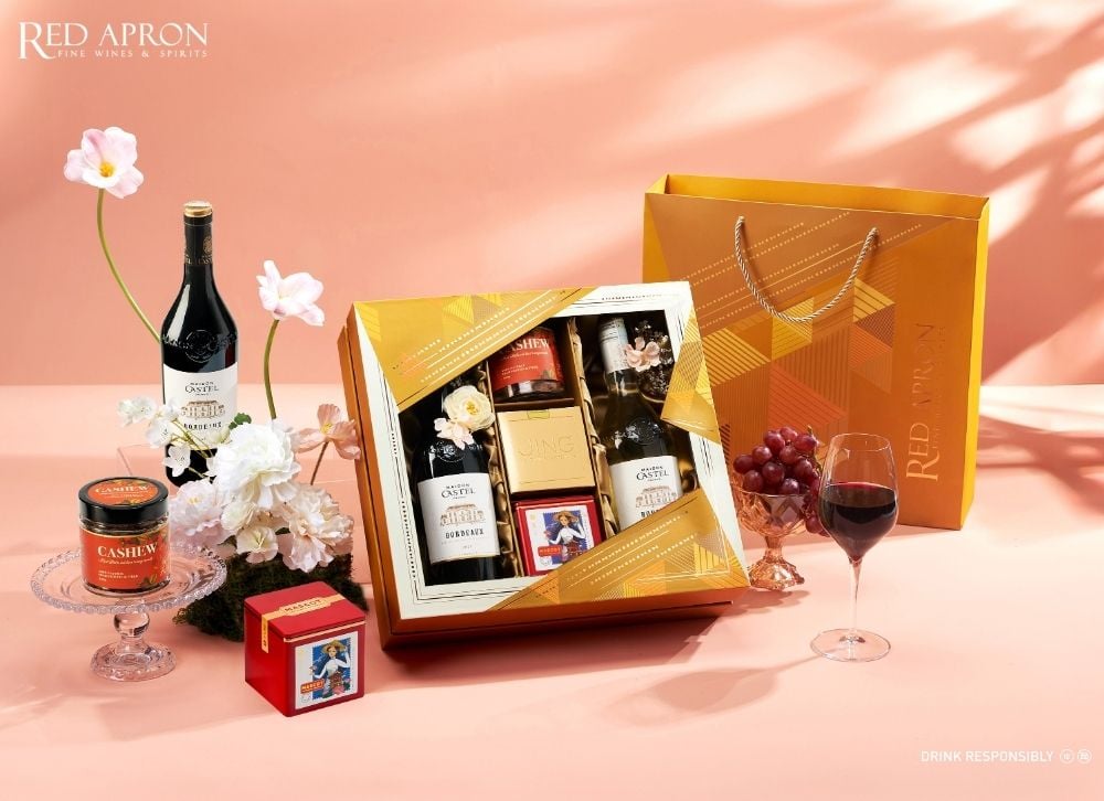 Ảnh flat lay set quà Tết tốt cho sức khỏe gồm chai rượu vang đỏ, hũ hạt điều, hộp quà và túi quà thương hiệu Red Apron, phù hợp biếu tặng doanh nghiệp và khách hàng cao cấp.