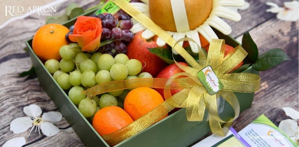 Cận cảnh hộp quà trái cây hữu cơ gồm chùm nho xanh, cam, lựu được gói nơ sang trọng, minh họa giỏ quà Tết tốt cho sức khỏe giàu vitamin và chất xơ.