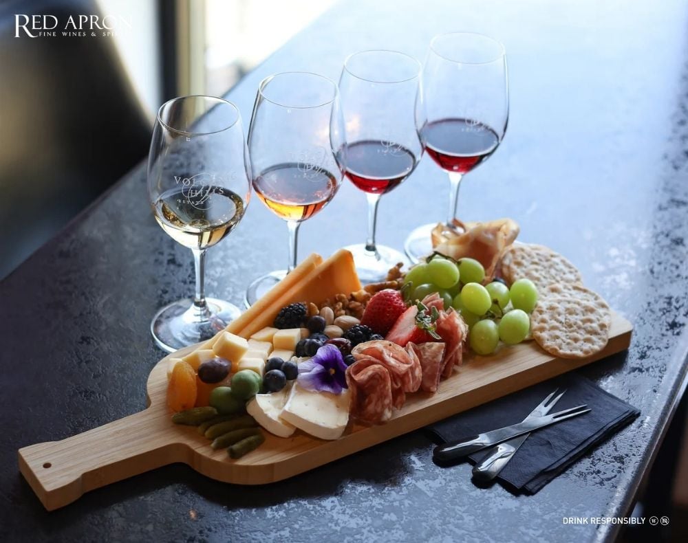 Đĩa phô mai bày trên thớt gỗ với nho, hạt óc chó và ly vang phục vụ đúng chuẩn