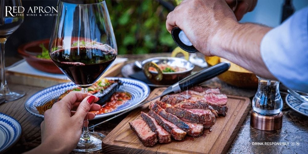 Ly rượu vang đỏ được rót cạnh món thịt nướng BBQ trên bàn ăn