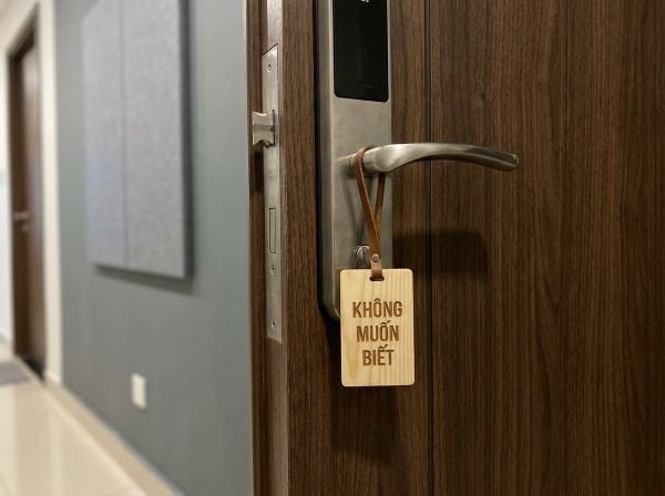 Biển báo tiếng Việt Không Muốn Biết treo trên cửa thép vân gỗ thể hiện sự từ chối tiếng ồn.