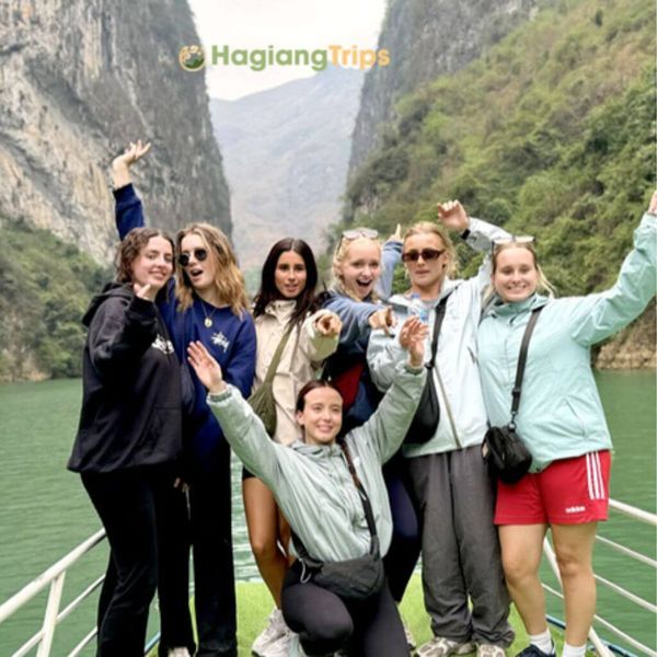 A cheerful group of female travelers posing on the deck of a boat cruising along the emerald green Nho Que River in Ha Giang.