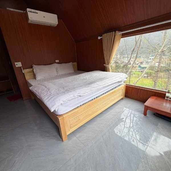 Cozy, wood-paneled bedroom at Nung homestay in Dong Van, featuring large glass windows that overlook a poetic mountain landscape