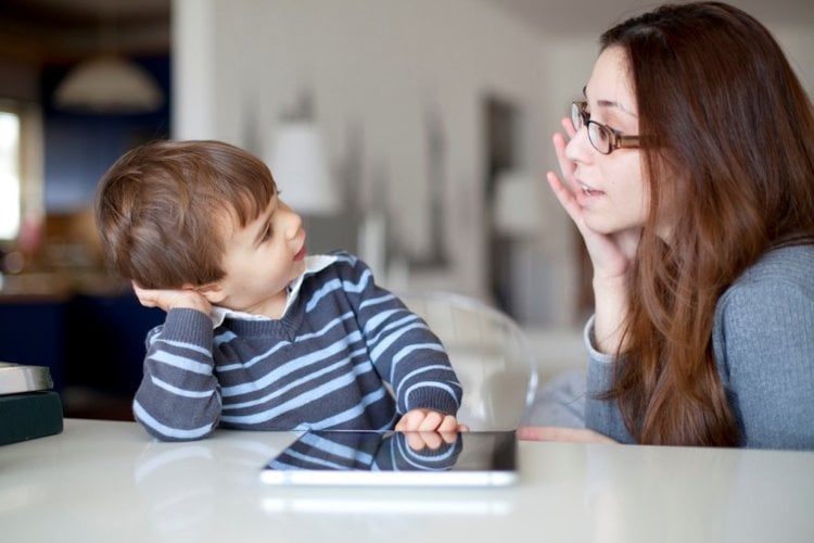 Bé trai dùng máy tính bảng bên cạnh mẹ đang quan sát
