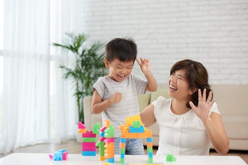 Bé trai và mẹ cùng cười khi xếp mô hình lego nhiều màu