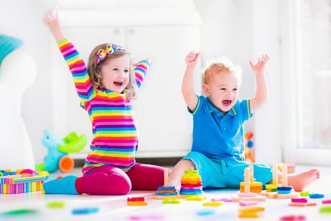 Hai bé nhỏ chơi với đồ chơi xếp hình nhiều màu trên sàn