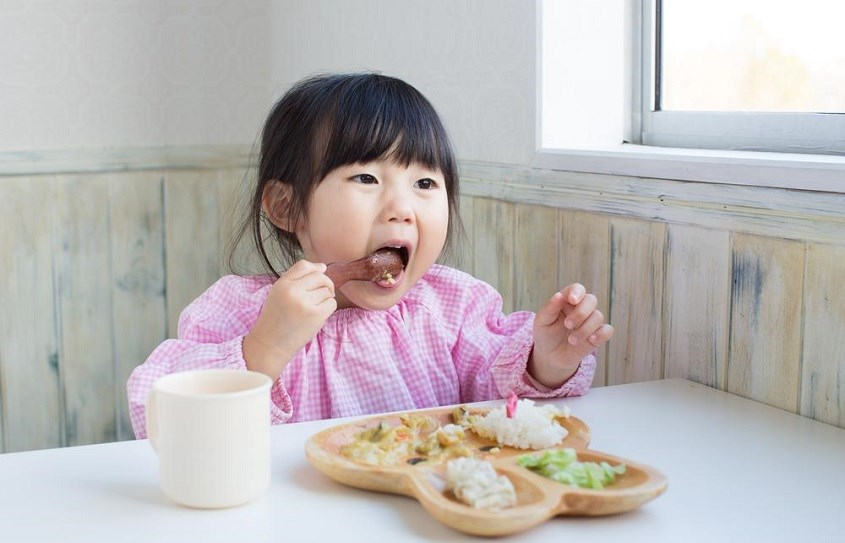 Bé gái tự xúc ăn bằng thìa tại bàn ăn