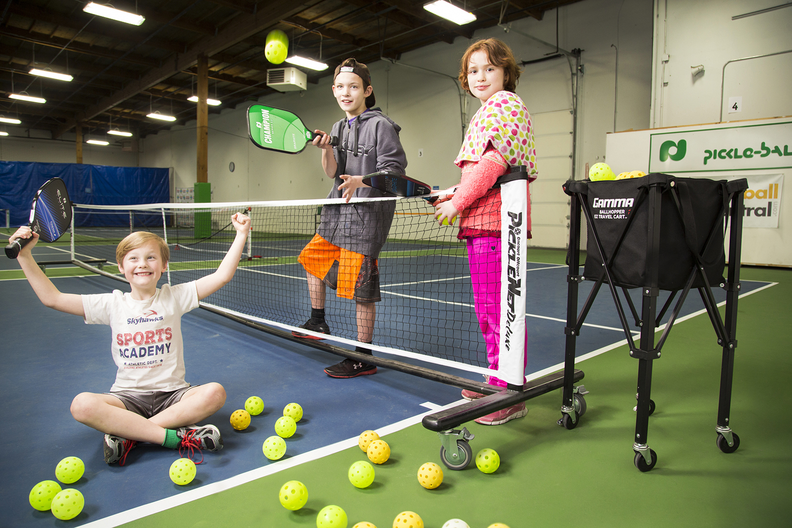 Trẻ tập tennis trong nhà thi đấu với vợt và rổ bóng
