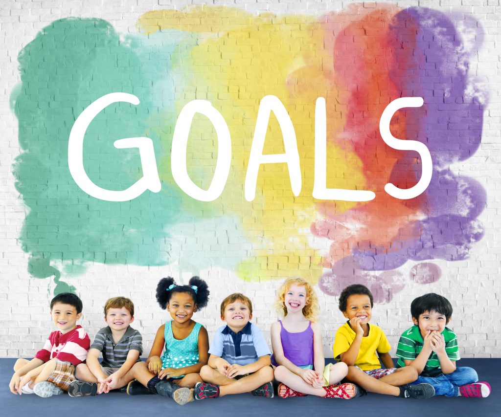 Nhóm trẻ ngồi trước bức tường vẽ chữ GOALS nhiều màu