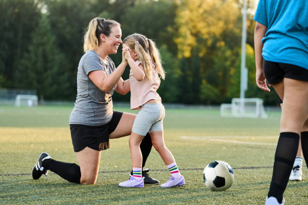 Huấn luyện viên quỳ xuống hướng dẫn bé gái trên sân bóng đá