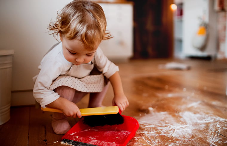 Bé nhỏ cầm xẻng chơi với bột mì vương vãi trên sàn bếp