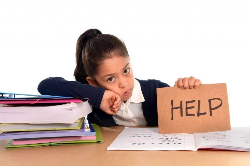 Bé gái ngồi trước chồng sách, giơ tấm biển ghi chữ HELP
