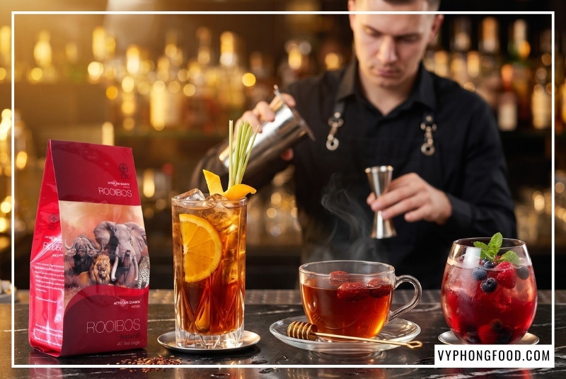 Gói trà rooibos nguyên liệu African Dawn nổi bật trên quầy bar bên ly trà cam sả và trà quả mọng rực rỡ.