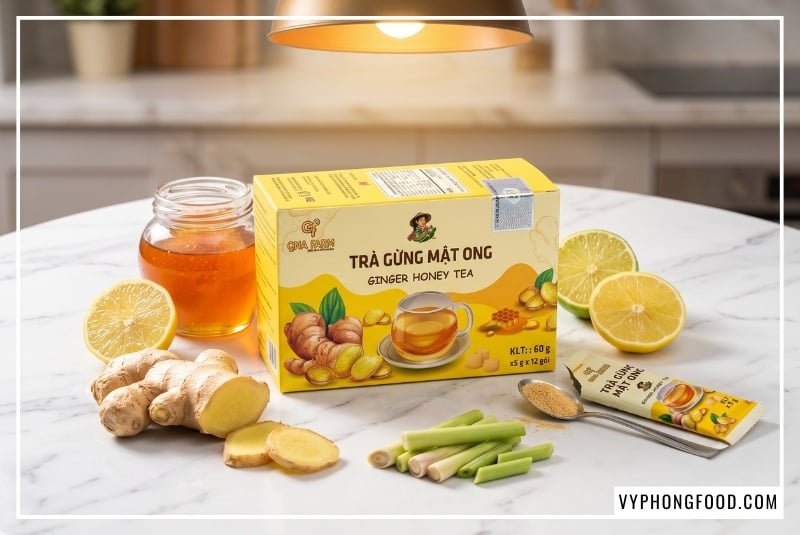 Vòng tròn nguyên liệu tự nhiên gồm gừng tươi, lát chanh, sả và mật ong bao quanh hộp trà gừng mật ong hòa tan QNA Farm 60g trên bàn đá cẩm thạch trắng, tối ưu hóa công cụ tìm kiếm cho từ khóa hướng dẫn làm trà gừng mật ong chuẩn vị.
