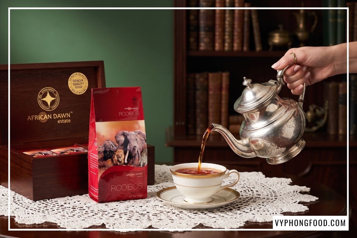 Rót hồng trà rooibos nóng vào tách sứ cạnh hộp quà sang trọng khi tham khảo bảng giá trà rooibos túi lọc cao cấp.