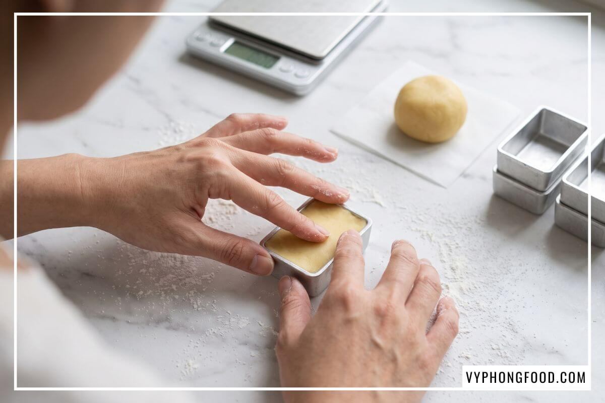 Mu bàn tay ấn bột bơ vàng mịn vào khuôn nhôm sắc nét theo đúng cách làm vỏ bánh dứa trên bàn đá cẩm thạch