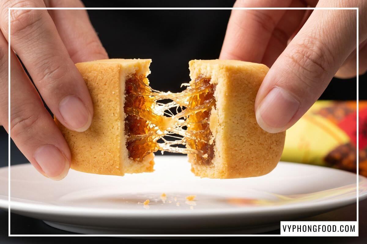 Hai bàn tay tách đôi chiếc bánh dứa Taiwan vàng xốp để lộ thớ nhân mứt dẻo óng ả trên đĩa sứ