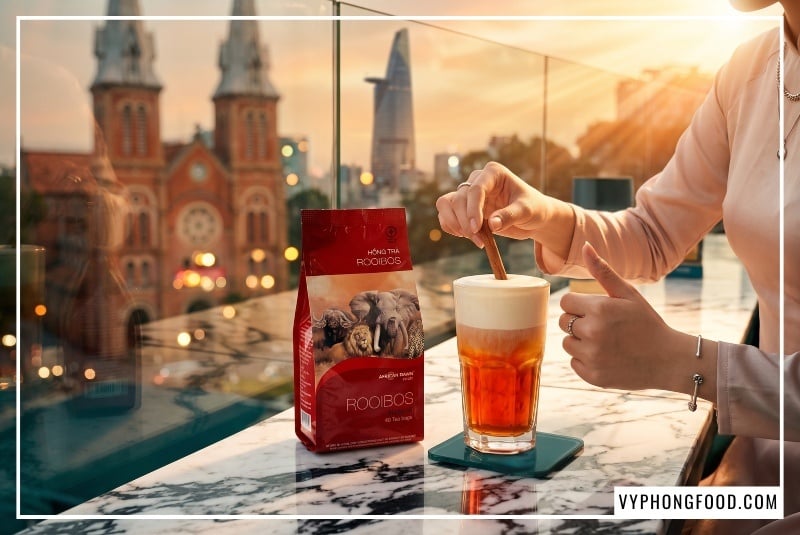 Bao bì Hồng trà Rooibos African Dawn màu đỏ ruby đặt cạnh ly trà sữa phân tầng bọt kem mịn màng trên bàn đá cẩm thạch tại ban công Katinat, đây là nguyên liệu làm trà sữa không caffeine tự nhiên giúp cả nhà ngủ ngon sâu giấc phân phối bởi vyphongfood.com.