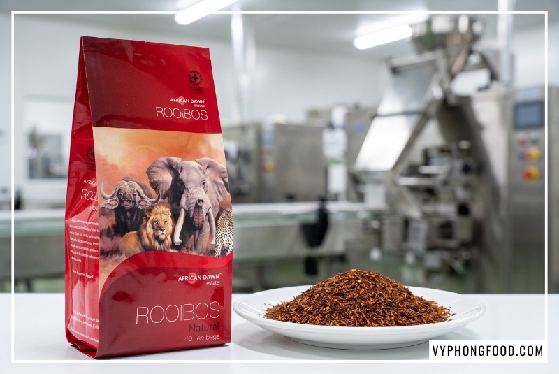 Cận cảnh gói trà African Dawn do Vy Phong Food bán sỉ hồng trà Nam Phi bên đĩa lá trà rooibos sấy khô đỏ nâu trong nhà máy đóng gói chuẩn quốc tế