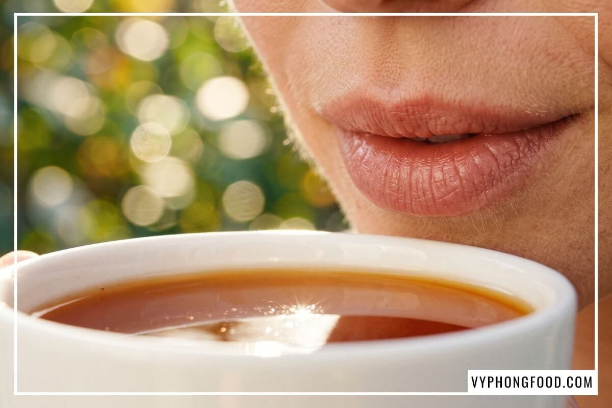 Môi nữ giới chạm sát mặt nước hồng trà rooibos trong tách sứ trắng dưới nắng xem uống trà có tốt cho sức khỏe không.