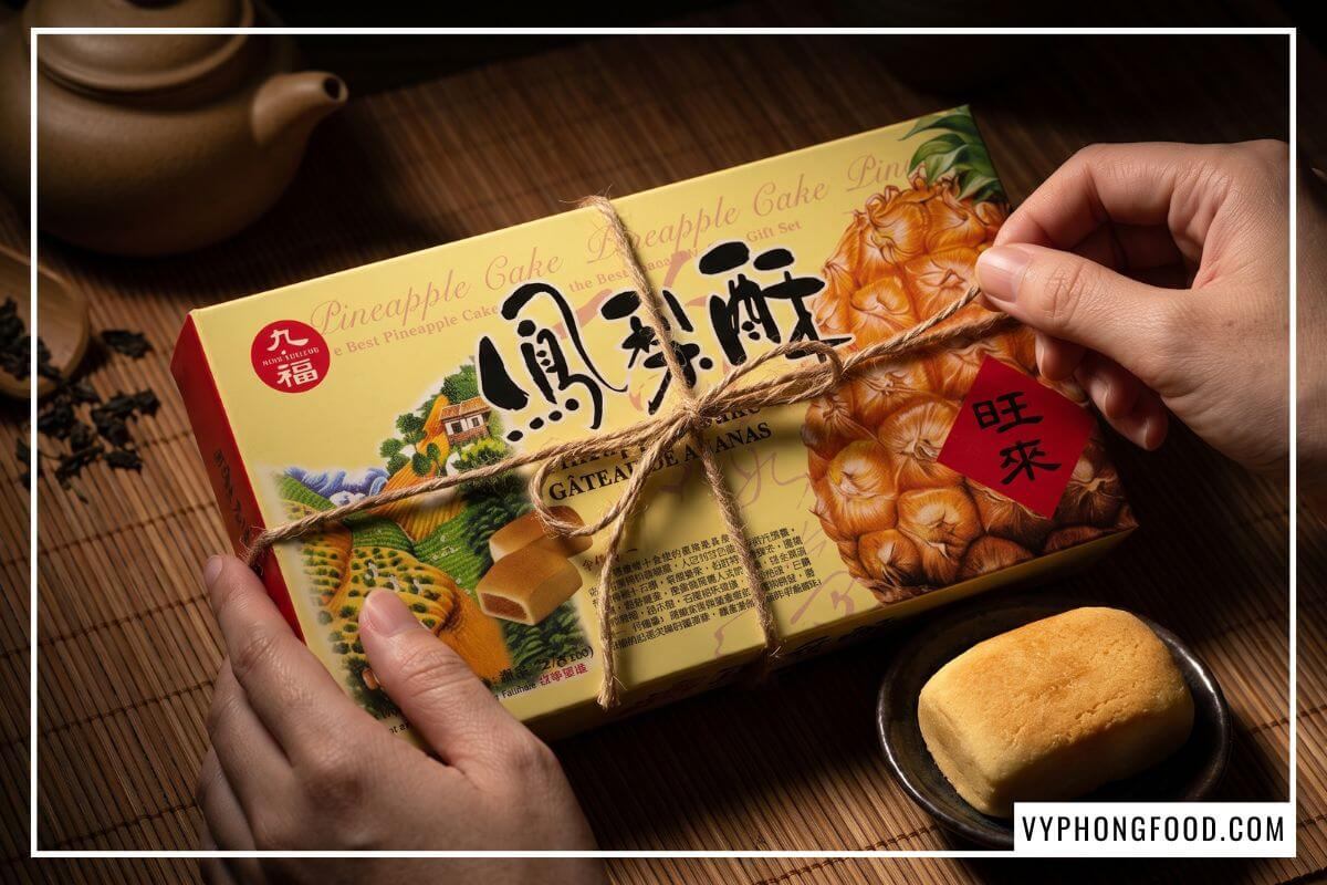 Hai tay nhẹ nhàng tháo dải ruy băng mở nắp hộp bánh dứa Nice Choice lộ ra những chiếc bánh nướng vàng ươm.
