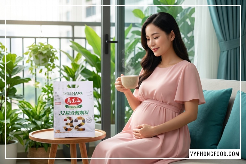 Góc chụp cận người mẹ bầu Việt Nam phúc hậu mỉm cười thanh tú, một tay nâng ly ngũ cốc ấm áp, tay còn lại đặt lên bụng bầu bên cạnh túi bột ngũ cốc dinh dưỡng không đường từ 32 loại hạt Greenmax Đài Loan đặt trên bàn trà ban công, chứng minh loại ngũ cốc nào tốt cho bà bầu.