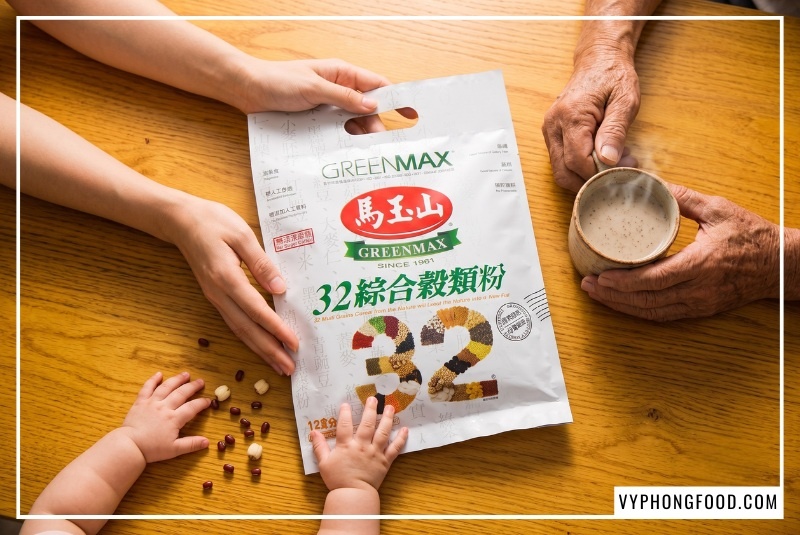 Túi bột ngũ cốc dinh dưỡng không đường từ 32 loại hạt Greenmax Đài Loan chính hãng tại Vy Phong Food nằm ở tâm điểm mặt bàn gỗ sồi, được bao bọc bởi đôi bàn tay chăm sóc của người mẹ, em bé và ly ngũ cốc ấm nóng của người ông, khẳng định giá trị gia đình từ các loại ngũ cốc tốt cho sức khỏe đa thế hệ.