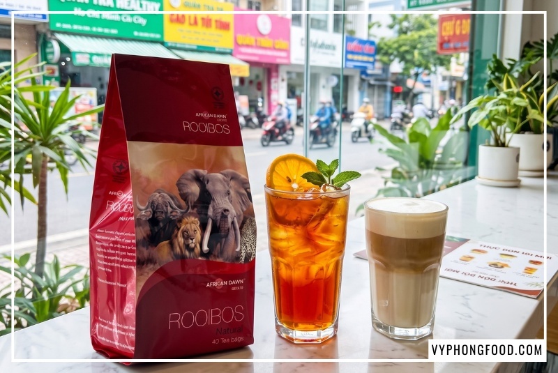 Ly trà ủ lạnh đặt cạnh gói sản phẩm hỗ trợ phối trộn trà thảo mộc rooibos sỉ cho quán cà phê.