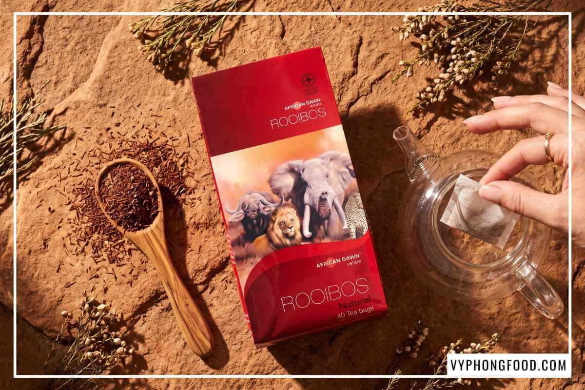 Gói hồng trà rooibos dạng túi lọc và muỗng gỗ đựng sợi trà khô đỏ nâu trên đá sa thạch