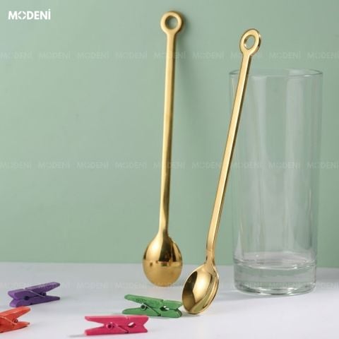 Góc chụp thẳng hai muỗng cafe Solis Gold Inox 304 màu vàng lấp lánh dựng tựa vào ly thủy tinh trong suốt trên phông.