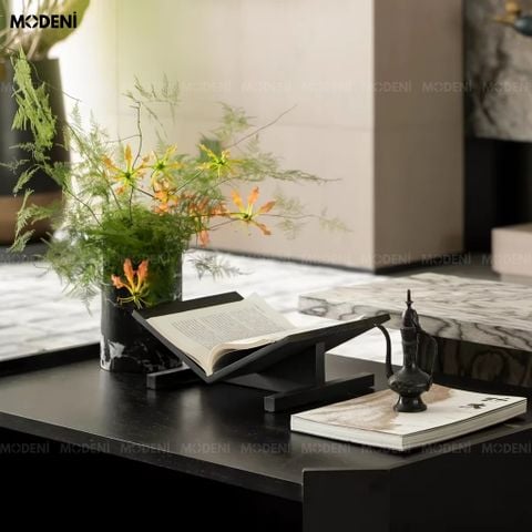 Góc chụp nghiêng trên mặt bàn làm việc, giá đỡ sách Novus nổi bật với màu gỗ đen nhám đang nâng đỡ một cuốn sách.