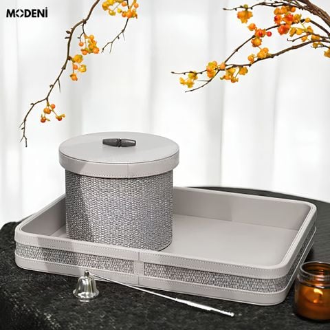 Tay người đang mở nắp hộp đựng mỹ phẩm Liora xám bọc vải nắp da khuy gỗ chống bụi, bên trong chứa chai lọ tinh dầu.