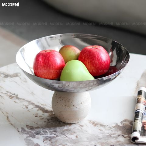 Góc nhìn chính diện tô trái cây thép không gỉ sáng bóng đế khối cầu composite đựng táo đặt trên bàn đá sáng màu.