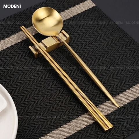 Gác đũa Riva Gold Inox 304 nguyên khối mạ vàng sáng bóng đặt trên tấm lót bàn ăn họa tiết ziczac.