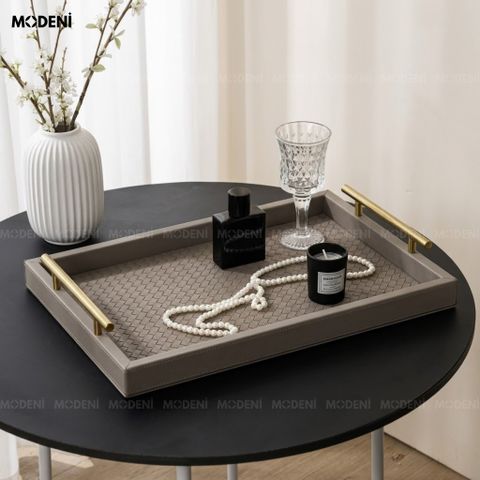 Góc chụp chéo trên bàn gỗ cạnh cửa sổ khay trang trí bàn trà bọc da màu xám họa tiết đan chéo đựng nến thơm và sách.