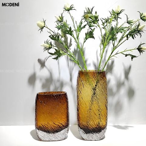 Bình hoa thủy tinh khối Amber Cube màu nâu vàng hổ phách cắm hoa tươi đặt trên mặt bàn phẳng.