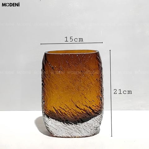 Bình hoa thủy tinh khối Amber Cube màu nâu vàng hổ phách cắm hoa tươi đặt trên mặt bàn phẳng.