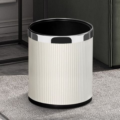 Thùng rác decor Vesta bọc da PU sọc dọc màu trắng be phối viền bạc chrome đặt trên thảm nỉ dệt xám cạnh sofa.