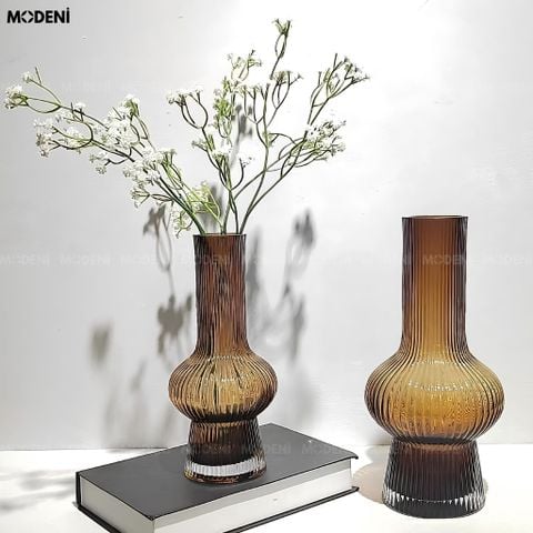 Góc chụp ngang hai bình hoa thủy tinh sọc gân màu nâu hổ phách thiết kế cổ cao, một chiếc đặt nằm trên mặt bàn trắng.