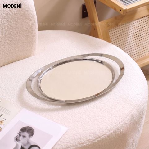 Khay trang trí Oval mặt da trắng be viền kim loại bạc đặt trên ghế đôn bọc lông cừu trắng cạnh cuốn tạp chí thời trang.