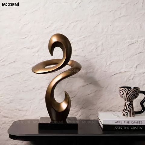 Góc nhìn chính diện tượng trang trí Helix composite nâu đồng trừu tượng đặt trên bàn cạnh cốc họa tiết vằn.