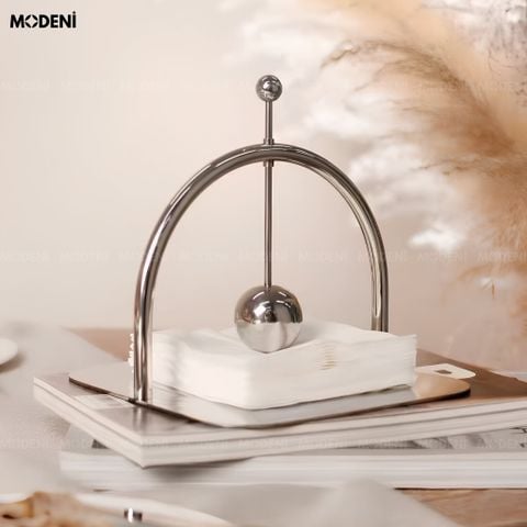 Góc chụp chính diện hộp khăn giấy chặn giấy ăn Vault bằng thép không gỉ màu bạc sáng bóng trên bàn ăn.