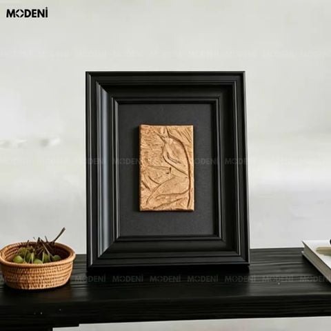 Trực diện trên bàn gỗ đen, tranh trang trí Tacet nổi bật với phần phù điêu vàng đồng tương phản hoàn hảo cùng khung đen.