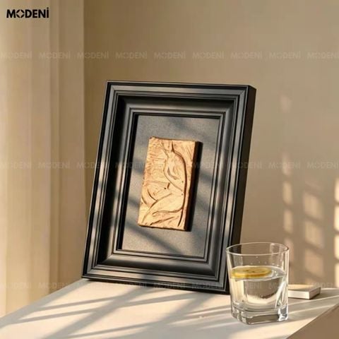Trực diện trên bàn gỗ đen, tranh trang trí Tacet nổi bật với phần phù điêu vàng đồng tương phản hoàn hảo cùng khung đen.