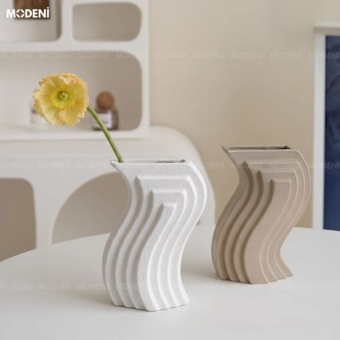 Trưng bày trên bàn tròn trắng, bình hoa Aero nổi bật với kiểu dáng sóng uốn lượn và bề mặt nhám lì cắm một bông hoa vàng.