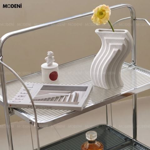 Trưng bày trên bàn tròn trắng, bình hoa Aero nổi bật với kiểu dáng sóng uốn lượn và bề mặt nhám lì cắm một bông hoa vàng.