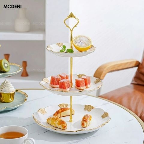 Cận cảnh bàn tiệc với Khay 3 Tầng Mariposa Sứ Trắng Phối Kim Loại trưng bày bánh ngọt và trái cây nổi bật lớp viền vàng.