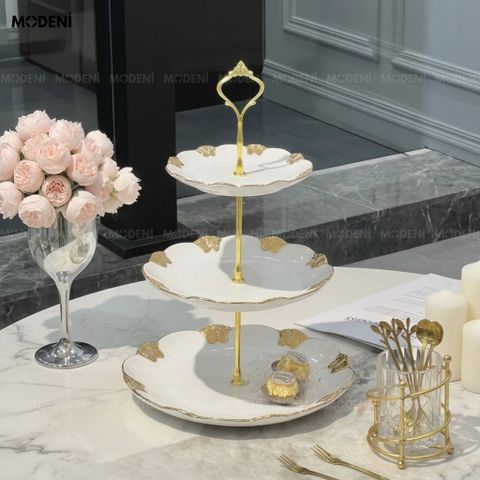 Cận cảnh bàn tiệc với Khay 3 Tầng Mariposa Sứ Trắng Phối Kim Loại trưng bày bánh ngọt và trái cây nổi bật lớp viền vàng.